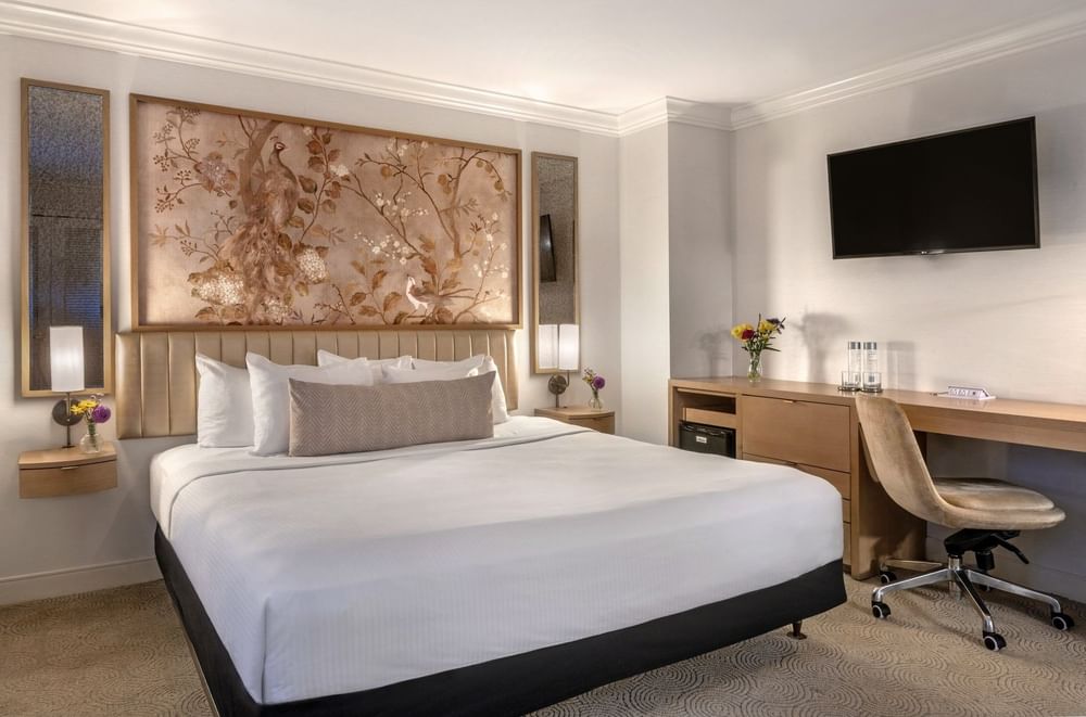 A cozy hotel room with a large bed, TV, and a desk with a chair at Warwick Allerton Chicago Redesign.