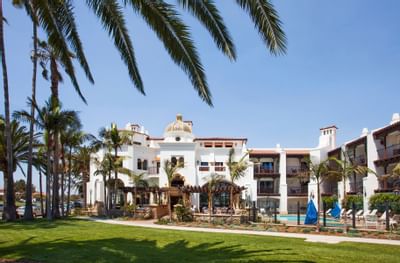 Scenic view Santa Barbara Inn Hotel with charming white stucco, palm trees, and a pool, under a clear blue sky
