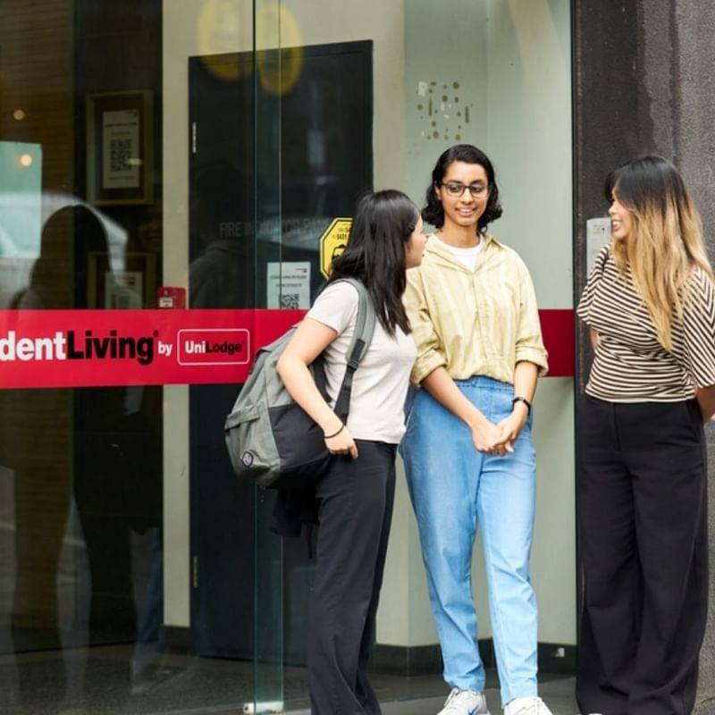 Three students chatting outside the entrance of a StudentLiving by UniLodge accommodation building.