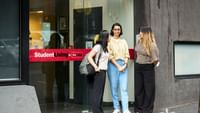 Three students chatting outside the entrance of a StudentLiving by UniLodge accommodation building.