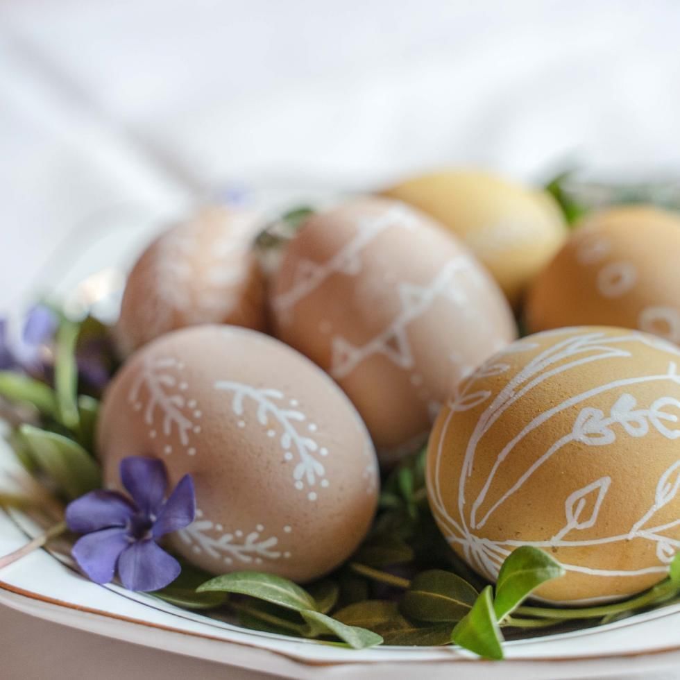Uova di Pasqua decorate con motivi floreali e fogliami freschi su un piatto