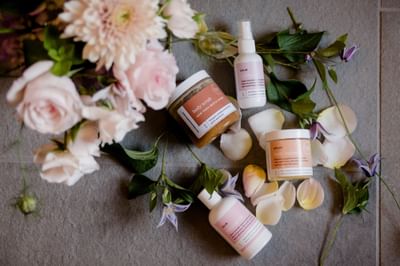 Aromatic body scrub and lotion bottles beside fresh flowers and soft petals on stone at La Tourelle Hotel and Spa