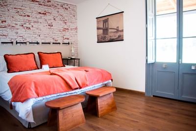 Bedroom with orange pillows and wooden stools by a brick wall under a bridge print at NOI Blend Colchagua, Valley