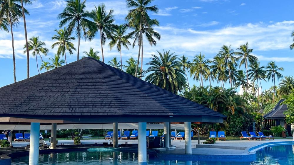 Large swimming pool with blue lounge chairs and palm trees at The Naviti Resort in Korolevu.