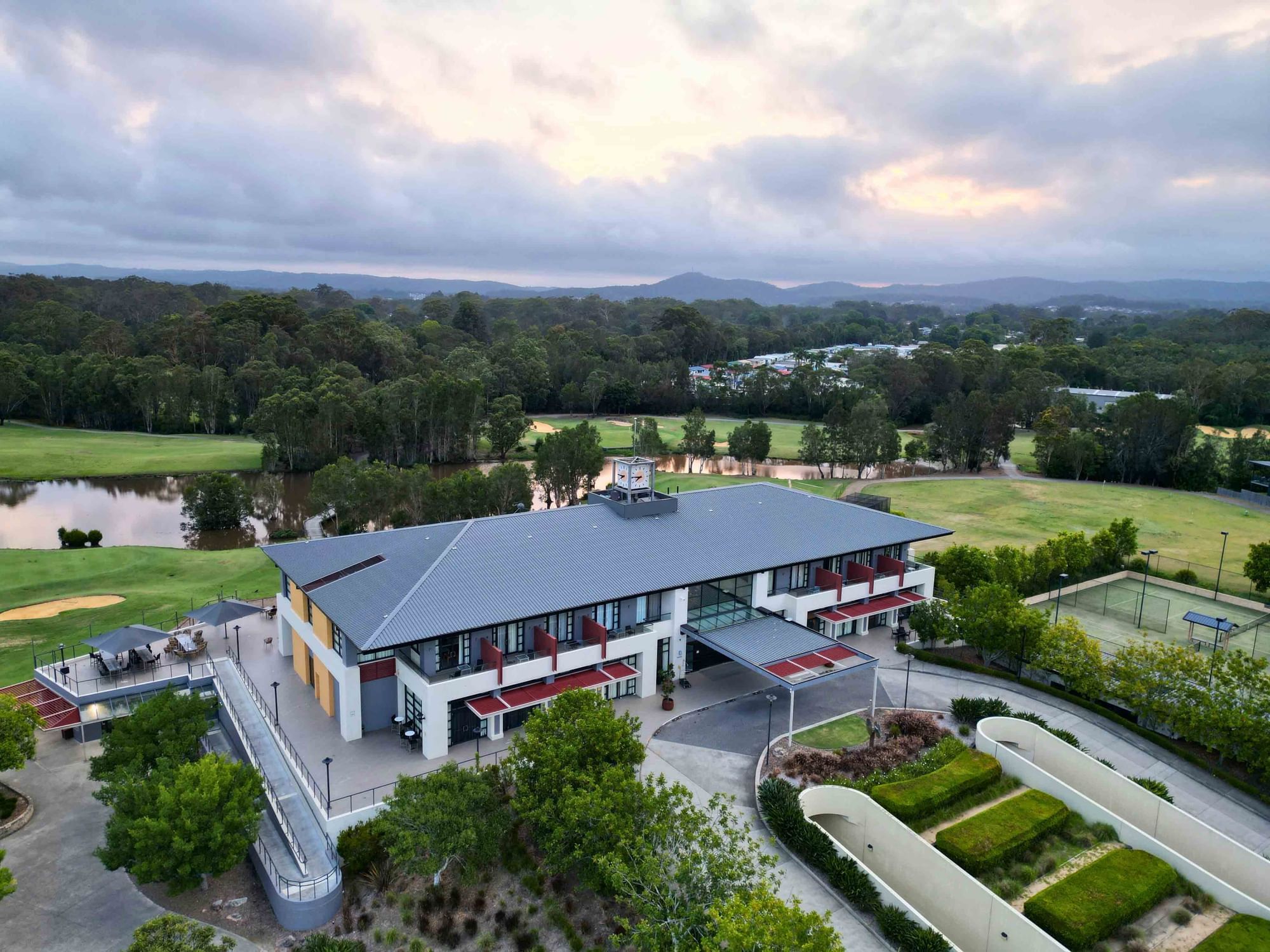 Aerial view of a modern building with a golf course and a water body in the background.