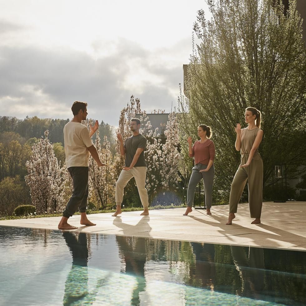 Vier Personen praktizieren Yoga am Pool während der Gesundheitswoche Be in Balance.