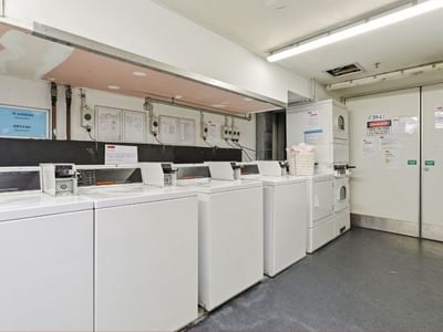 White washing machines and dryers in a laundry room at Student Living Auckland – Anzac.