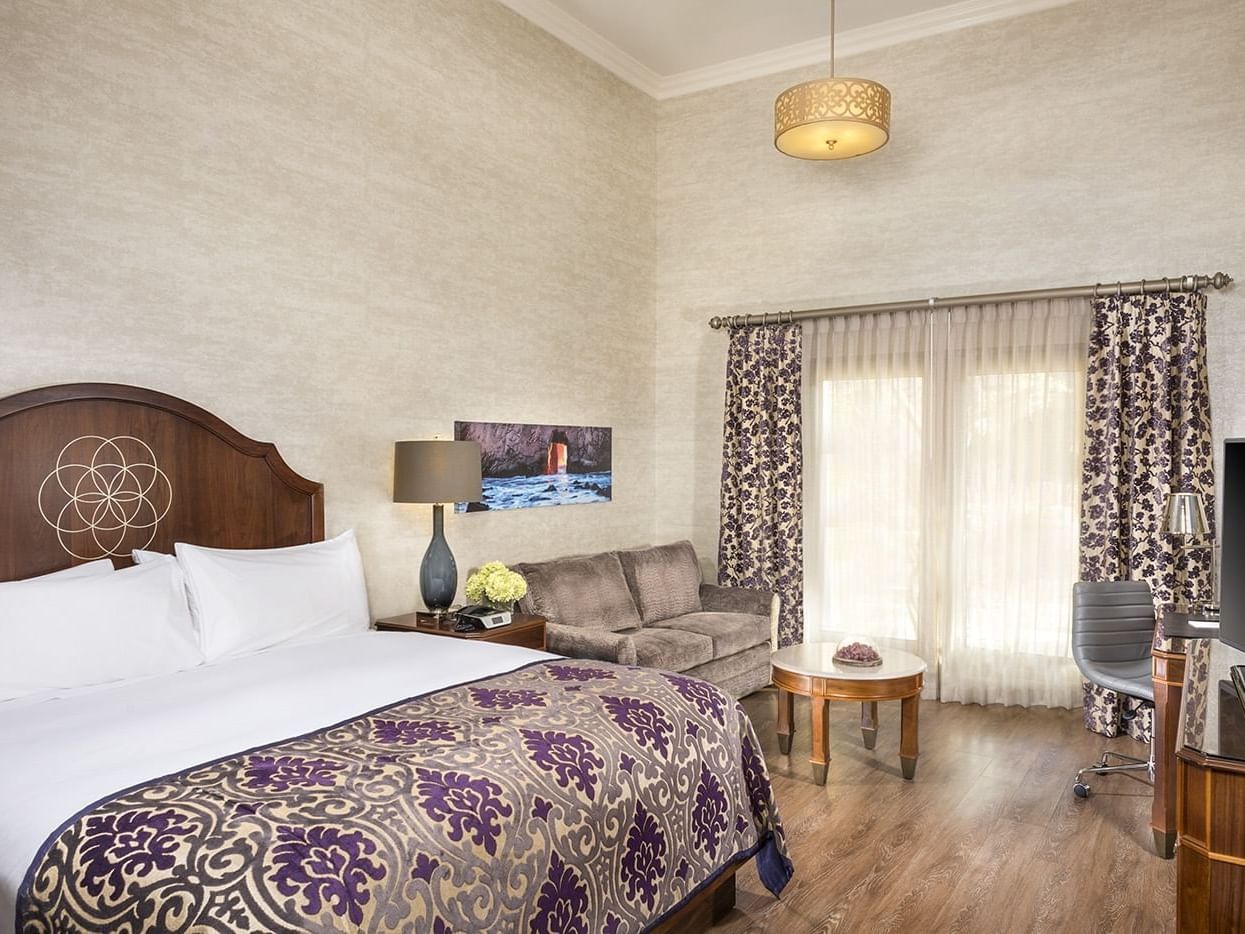 A room which includes a king size bed, sofa and coffee table, a writing desk and a flat screen TV.