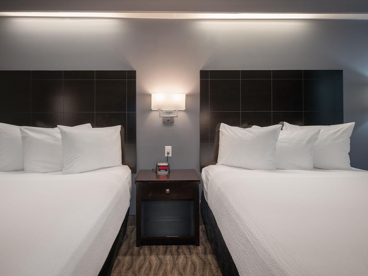Two queen beds with white linens and pillows in a hotel room.