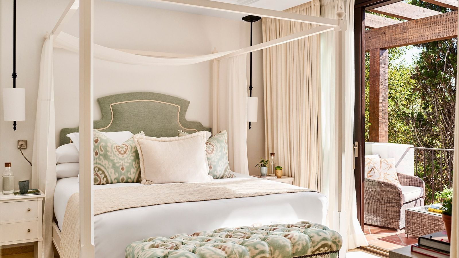 La Concha Suite with four-poster bed with a sage green headboard, tufted bench, & glass doors at Marbella Club