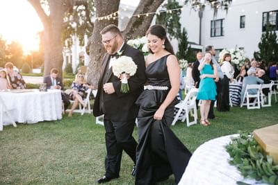 Elegant wedding party couple walking through an outdoor evening reception lawn at The White House Hotel