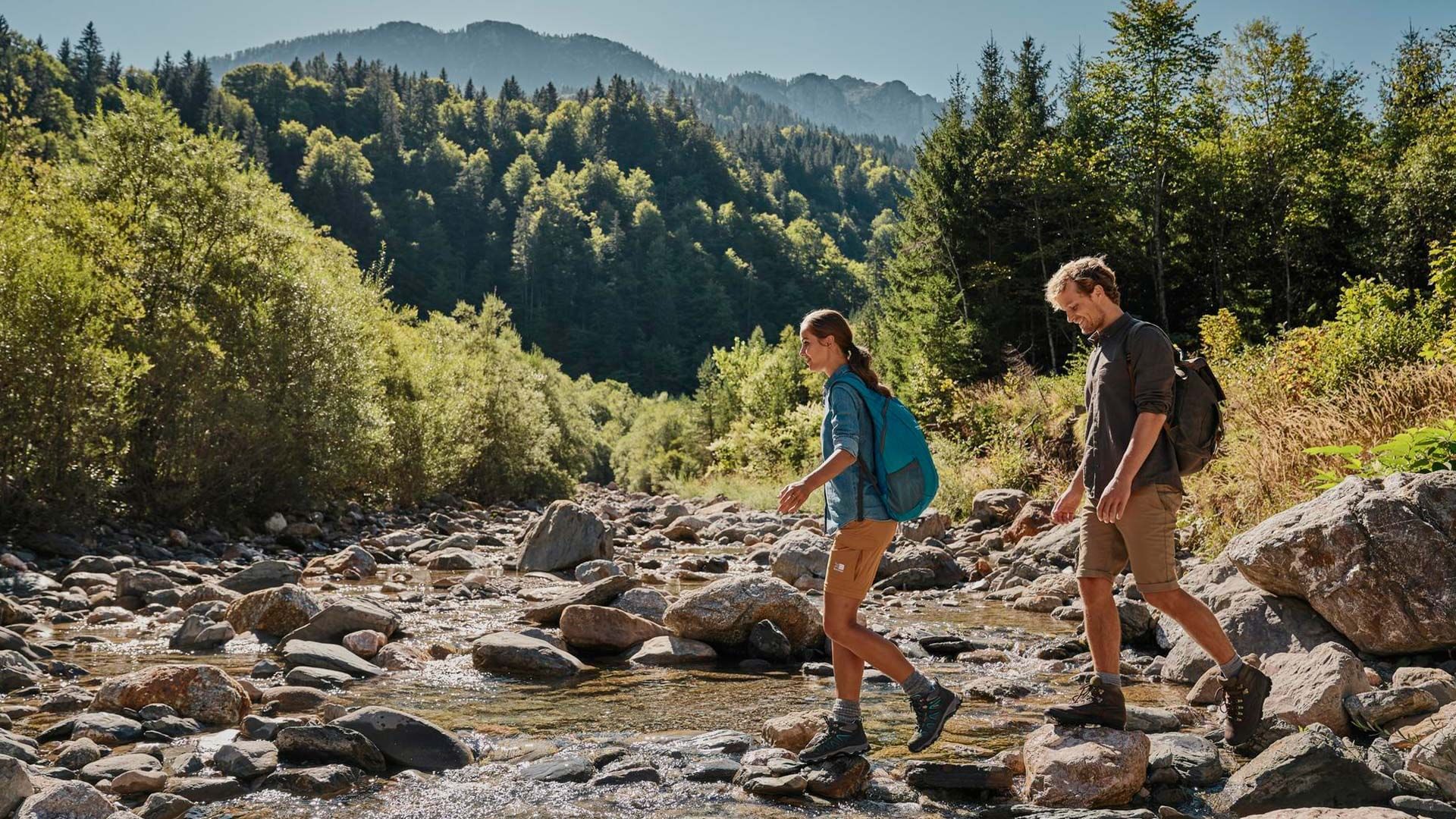 Hiking couple wading across a rocky river, Falkensteiner Hotels