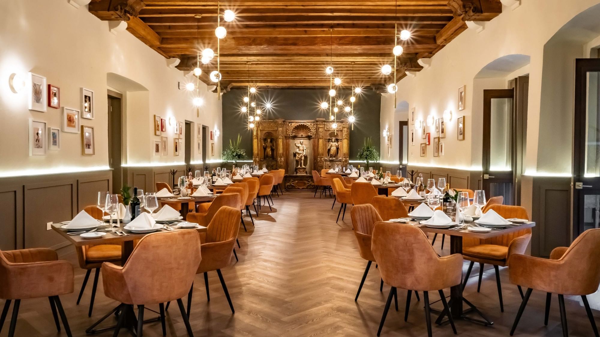 Amplio comedor de hotel con sillas naranjas, vigas de madera y luminarias de esferas en Quinta Real Puebla