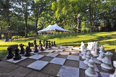 Large chess pieces and a board beside a lawn facing a white tent and trees at Avon Old Farms Hotel