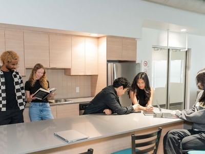 Students studying and socializing in a bright communal kitchen with large island and modern stainless steel appliances.