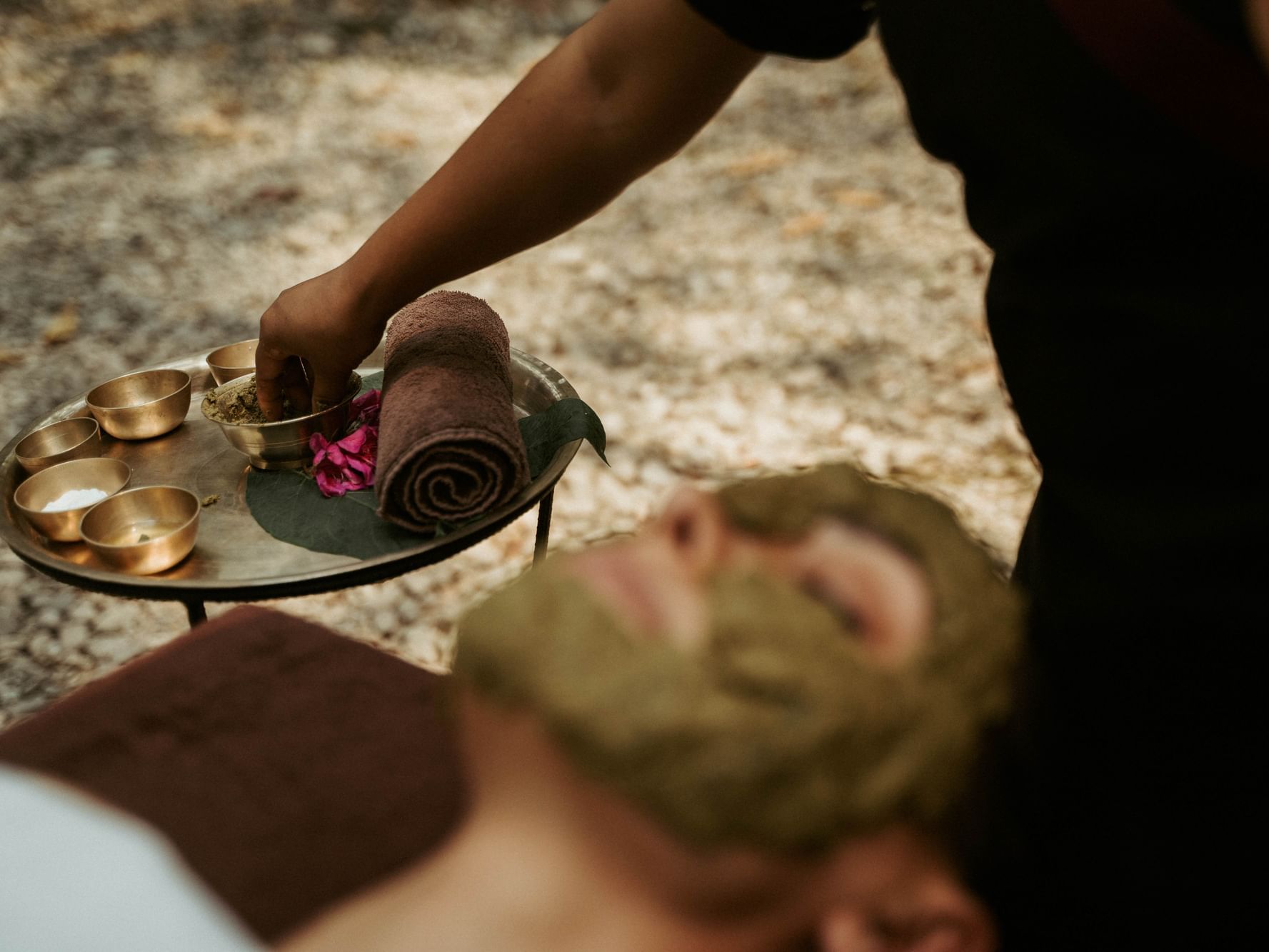 Person having a facial amid natural elements, with a tray of herbal ingredients at Dwarika's Himalayan Wellbeing