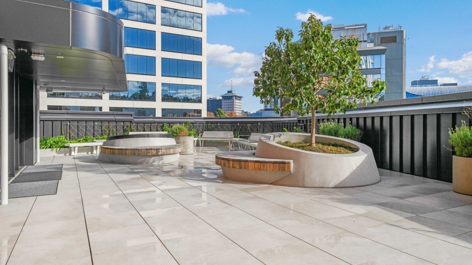 Modern rooftop terrace with curved planters, wooden benches, and city skyline views at UniLodge Auckland Central.