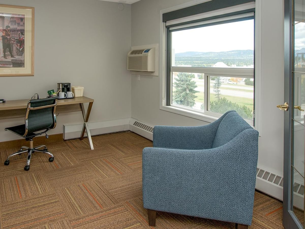 Coast Suite with blue armchair, wooden desk, and mountain view window.