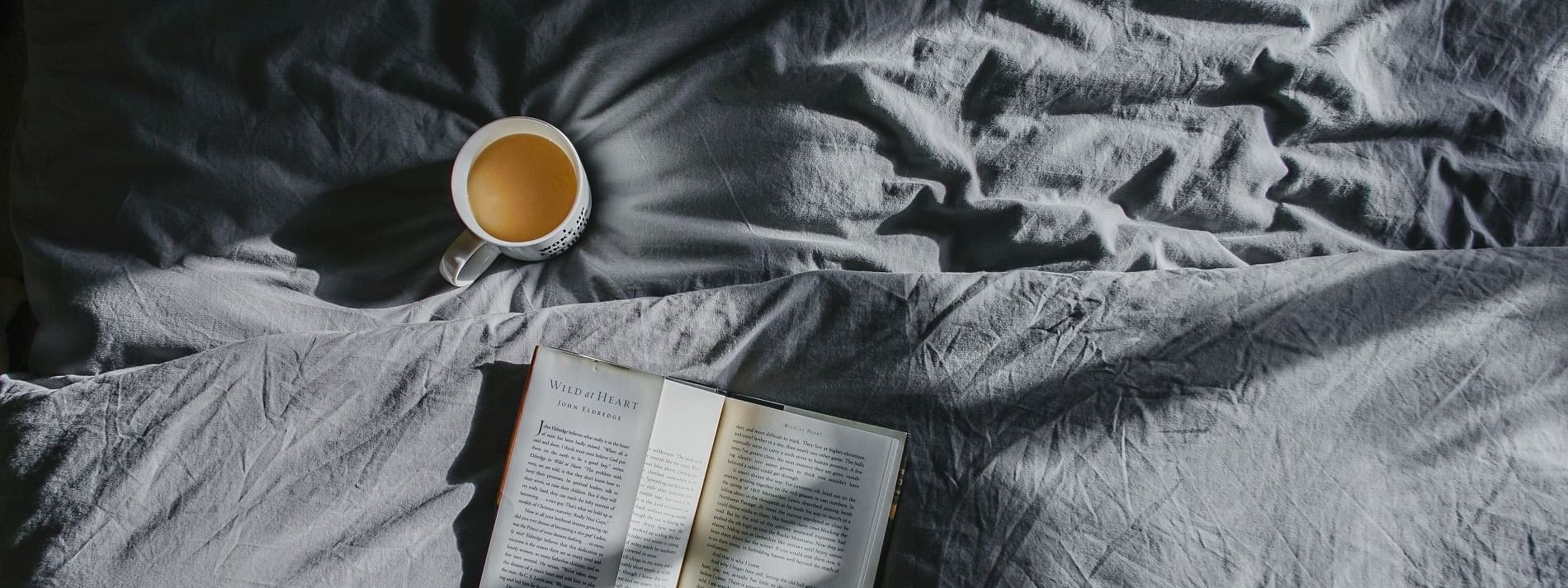 Cup of a tea and a book on a bed at Crown Hotels