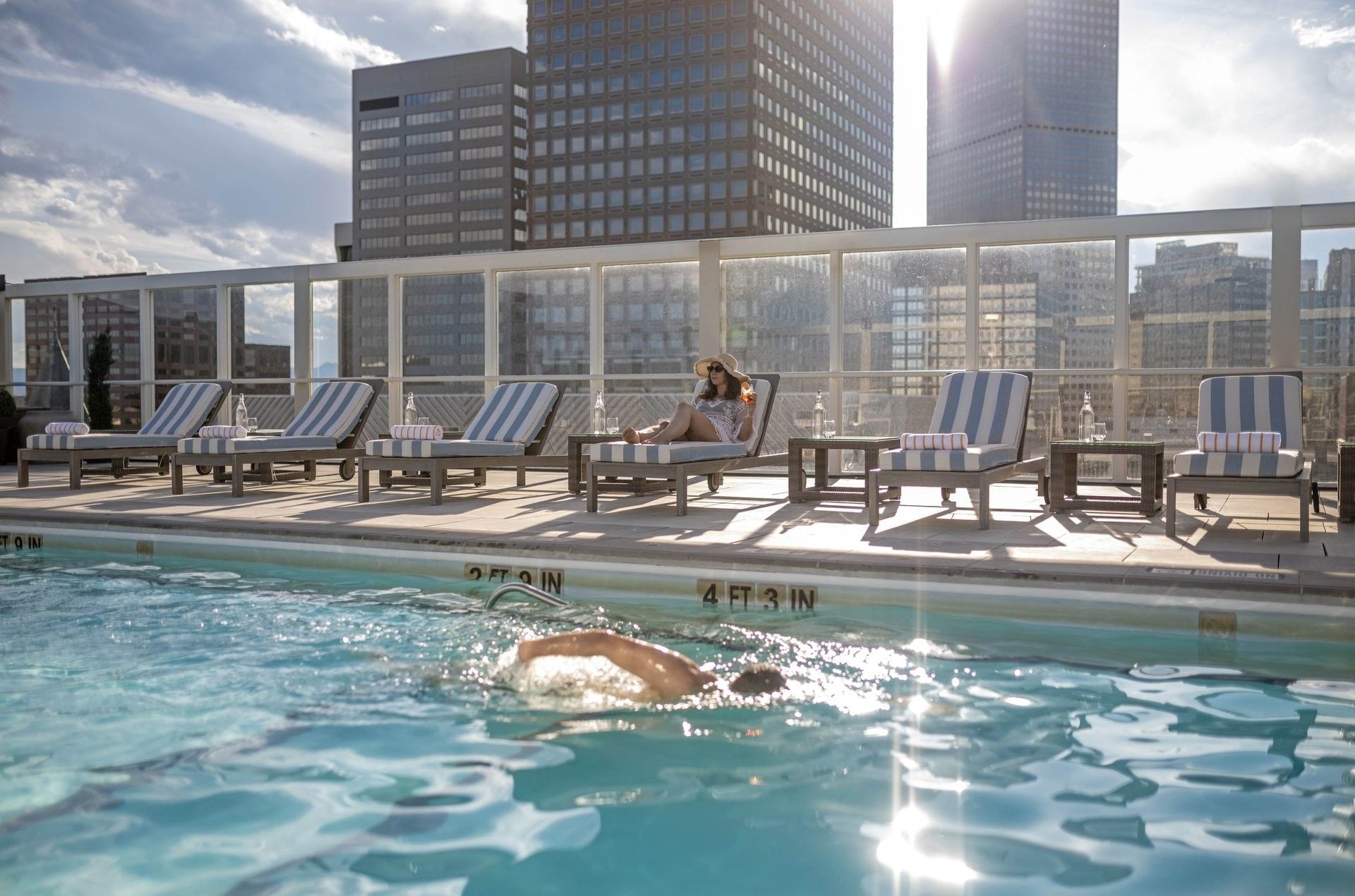 A rooftop pool with a swimmer and lounge chairs, overlooking the city skyline.