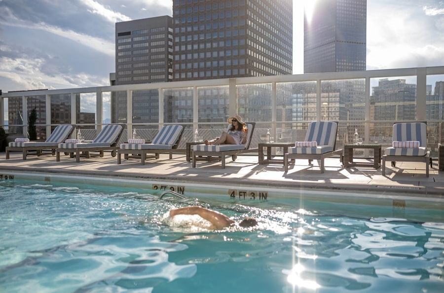 Guest swimming in the rooftop pool near loungers under the bright sun at Warwick Denver