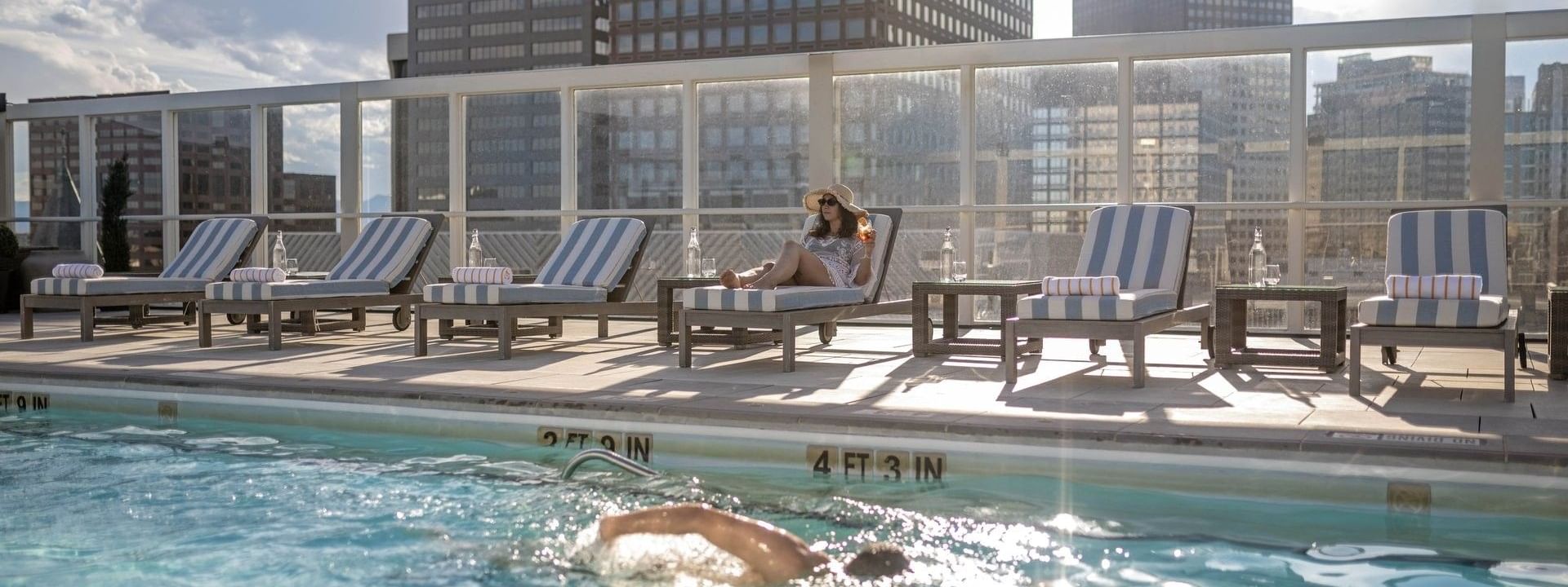 Guest swimming in the rooftop pool near loungers under the bright sun at Warwick Denver