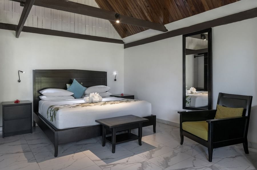 Modern bed with a black headboard and a dark armchair in Garden View Villa at Tambua Sands Beach Resort