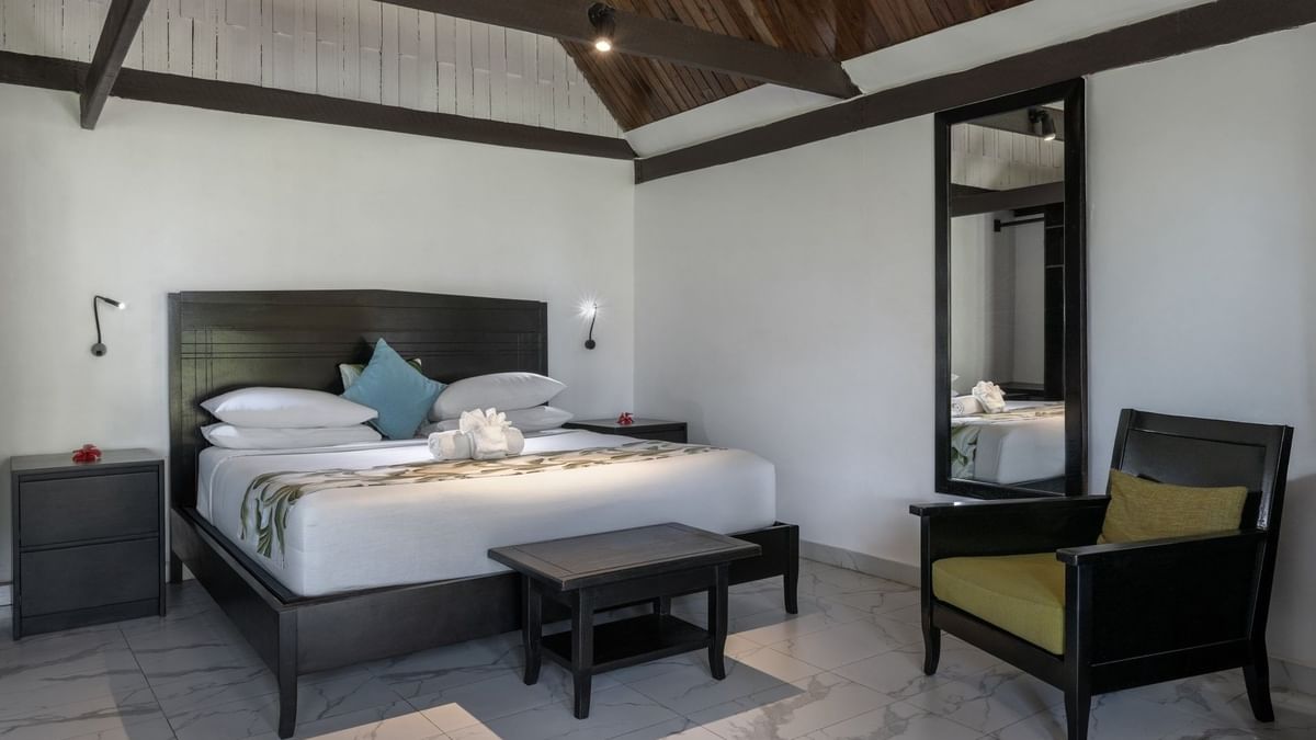 Modern bed with a black headboard and a dark armchair in Garden View Villa at Tambua Sands Beach Resort