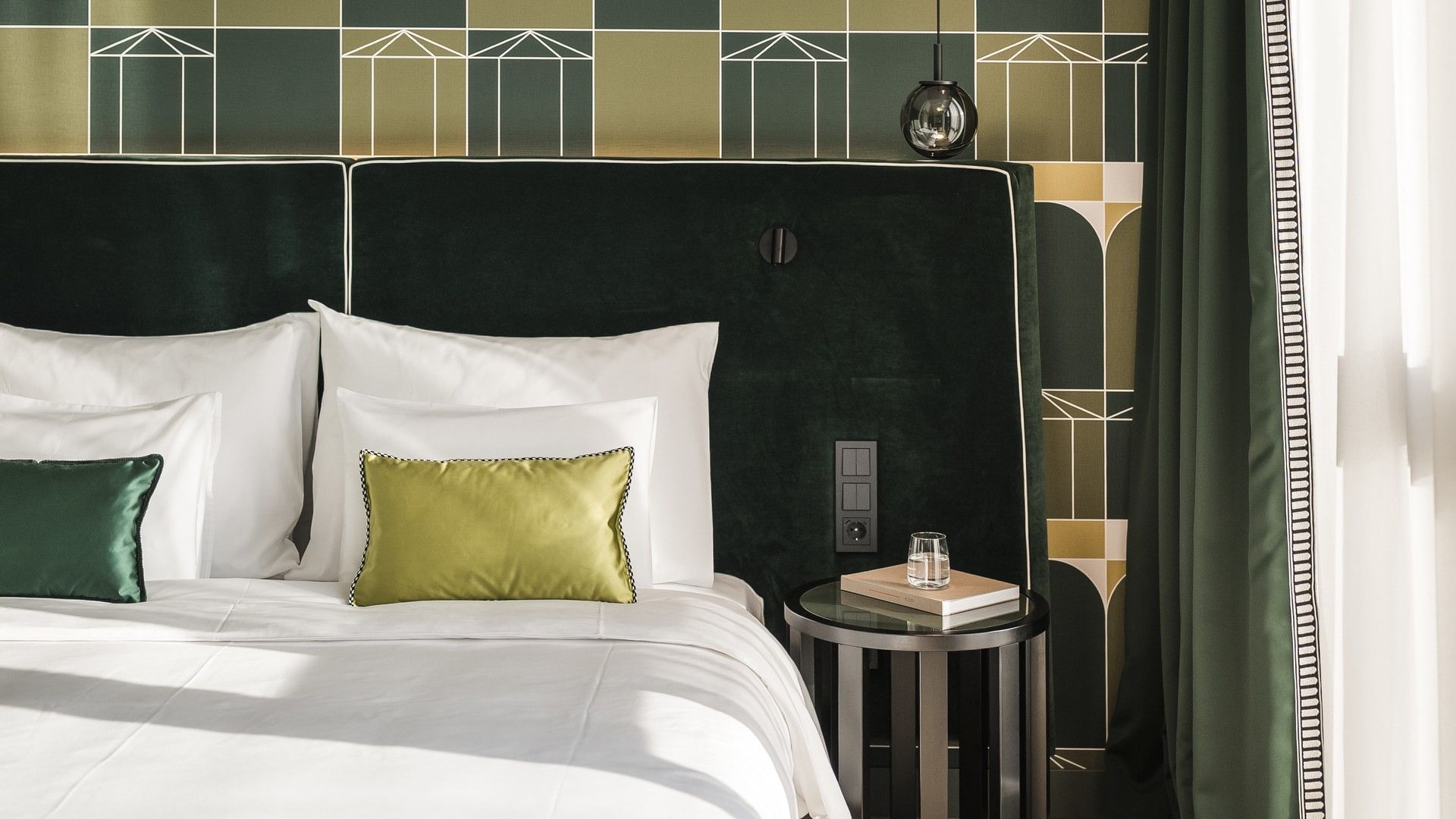 Elegantes Schlafzimmer mit grün gepolstertem Bettkopfteil, weißen Kissen, und einem Nachttisch mit Buch.