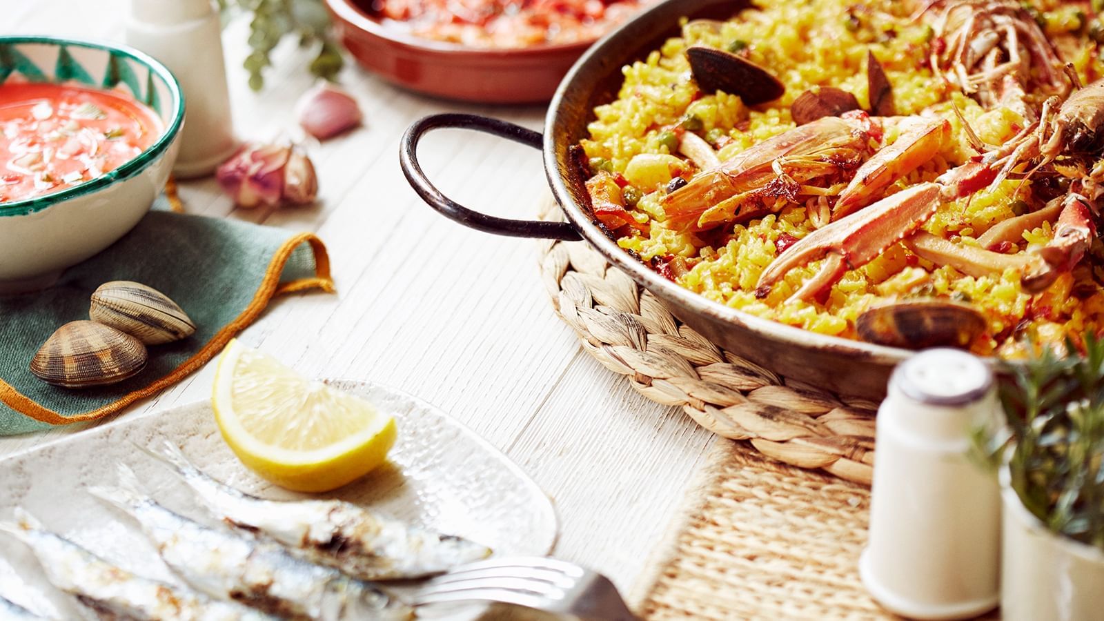 Close-up of paella in a pan and grilled sardines placed on a plate with a lemon served at Marbella Club
