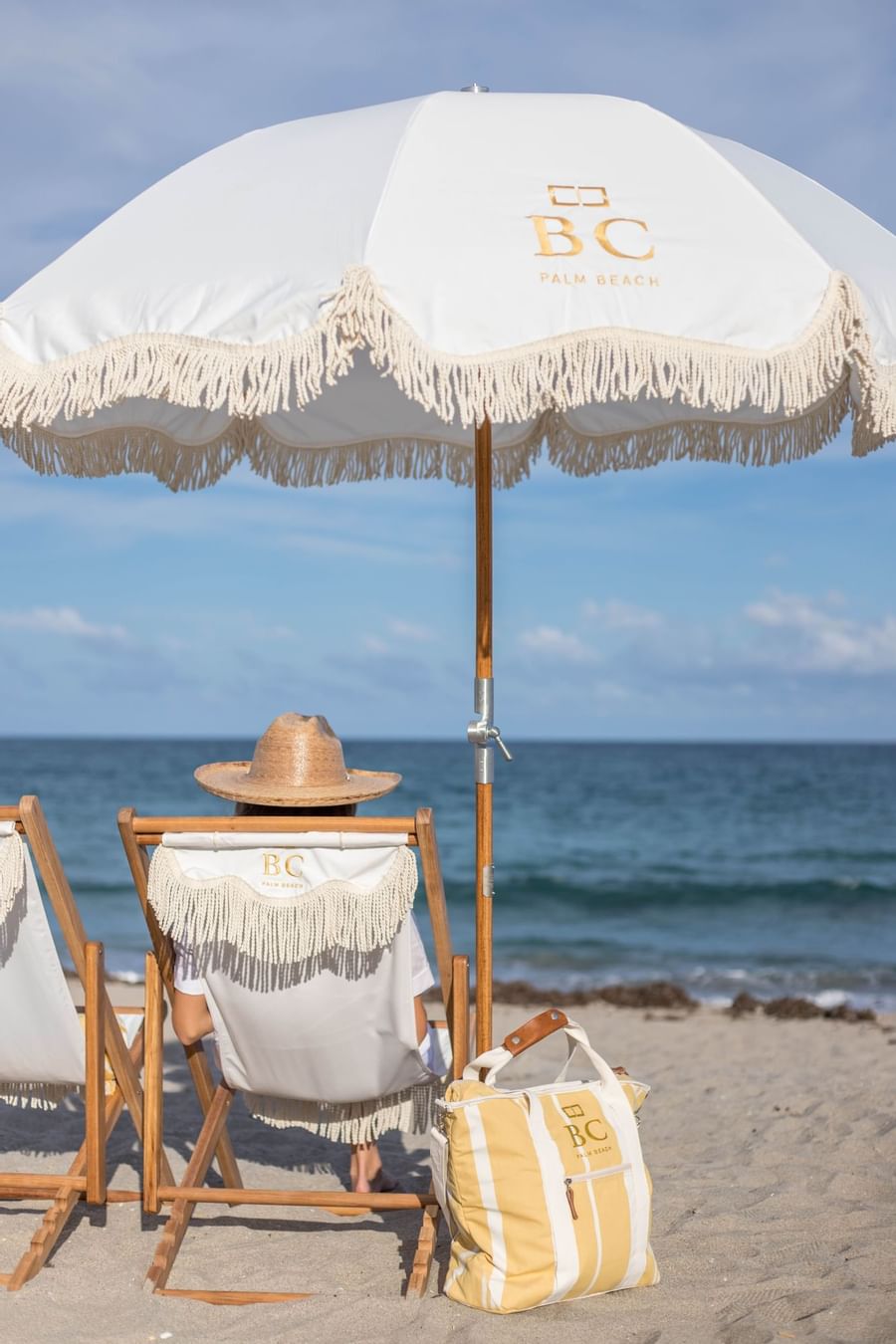 Woman in sun hat sitting under fringed beach umbrella on lounge chair at oceanfront near The Brazilian Court