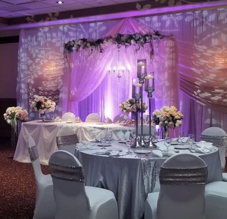 Round table with silver linens by tall candle centerpieces, under a pink draped backdrop at Glenmore Inn & Convention Centre