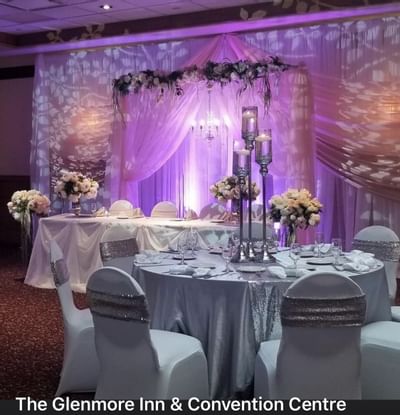 Round table with silver linens by tall candle centerpieces, under a pink draped backdrop at Glenmore Inn & Convention Centre