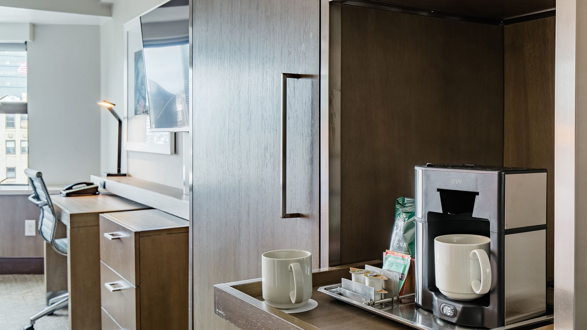 A hotel room with a coffee maker, desk, chair, and TV.