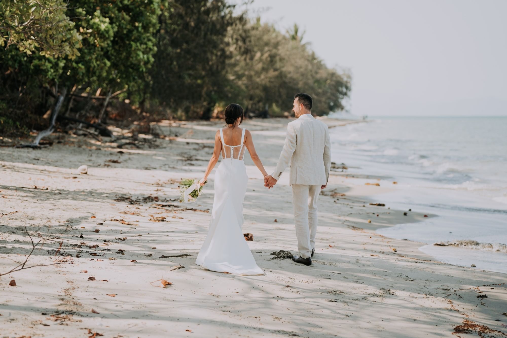 Bride and groom walking on beach with holding hands at Pullman Port Douglas Sea Temple Resort & Spa