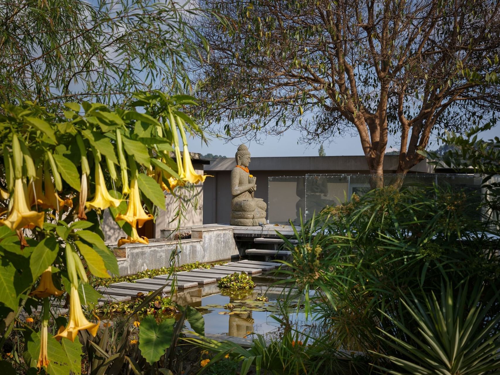 A tranquil garden with a Buddha statue, hanging flowers, and lush greenery at The Terraces Resort & Spa