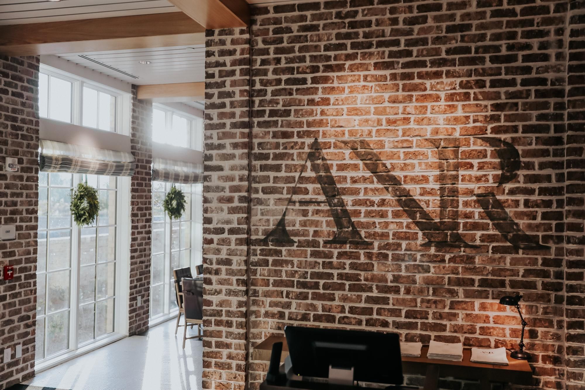 Brick wall with large ANR letters, adjacent to a bright room with windows and greenery.