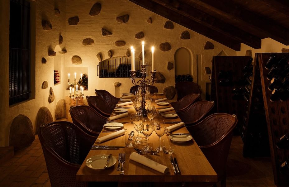 Long dining table set for dinner with wine glasses and candles in a cozy wine cellar at Kokkedal Slot Copenhagen by Warwick