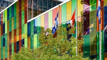 Flags flying by a facade of colorful glass panels at the convention center near Warwick Le Crystal Montreal