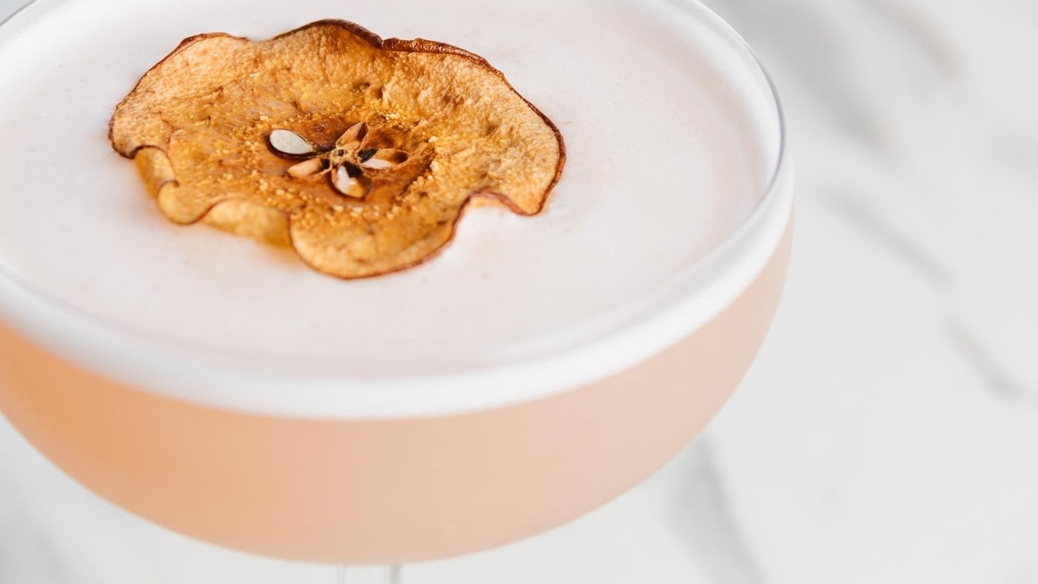 Cocktail at Mauad Hotel, with a light pink liquid topped with foam and a dried apple slice in Bistro Manly
