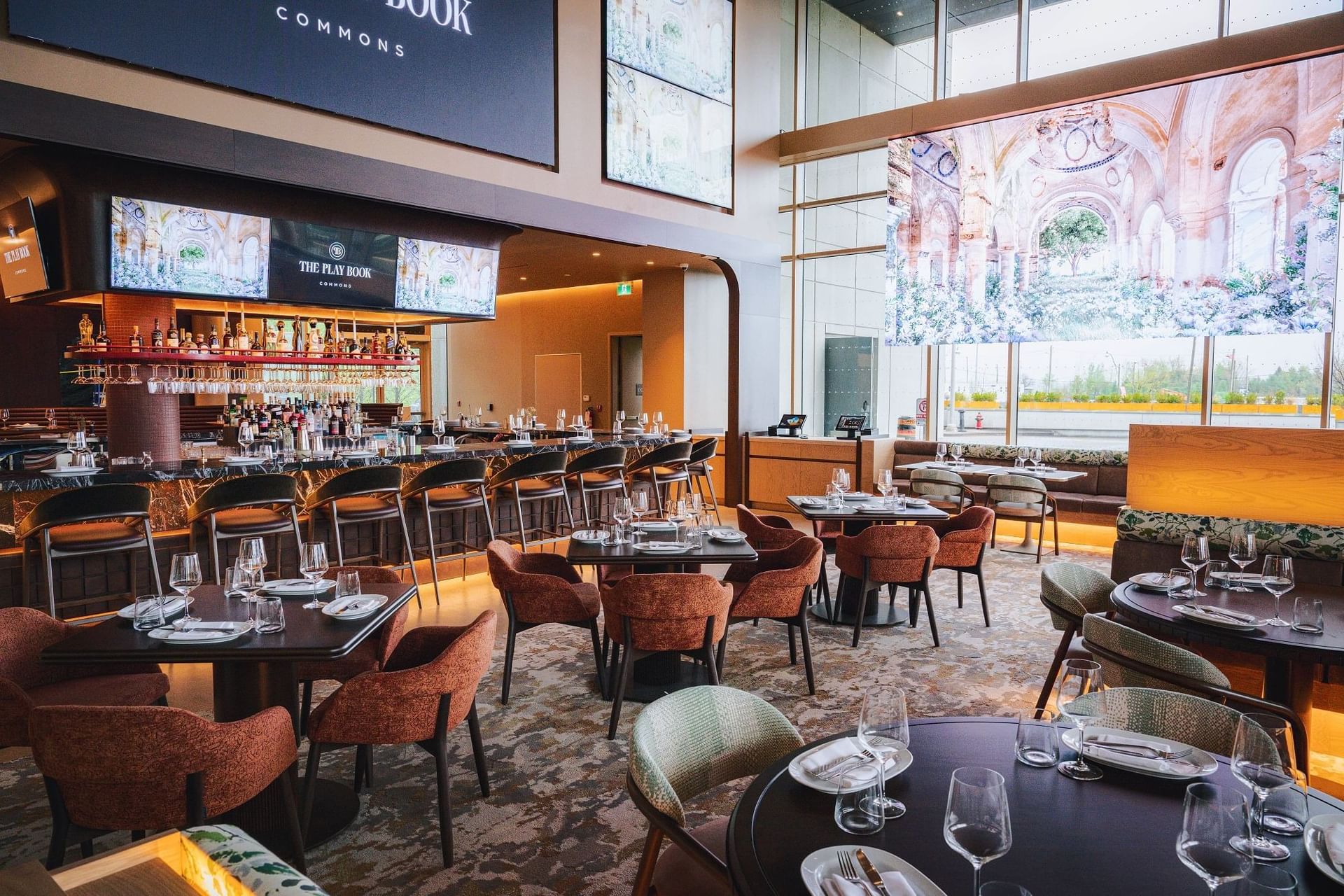 The Playbook Commons bar and restaurant with clean round dining tables and plush armchairs inside luxury Hotel X Toronto