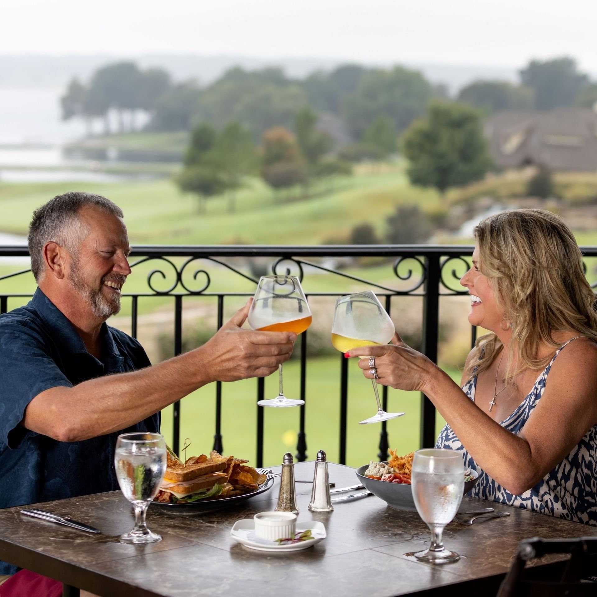 Smiling couple toasting with wine glasses while dining on a balcony at Shangri-La Resort and Golf Club