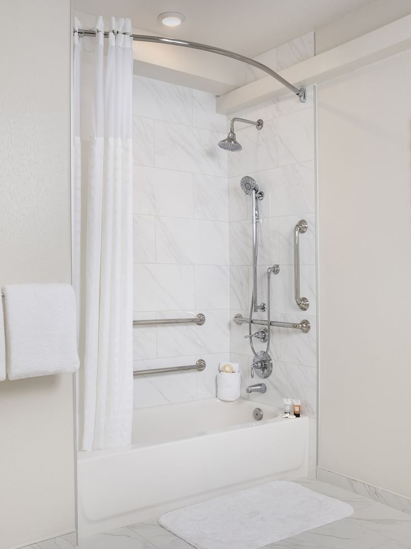 Bathtub with grab bars by a white curtain under a tiled wall in Classic Double Accessible at Warwick Melrose Dallas