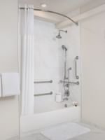 Bathtub with grab bars by a white curtain under a tiled wall in Classic Double Accessible at Warwick Melrose Dallas