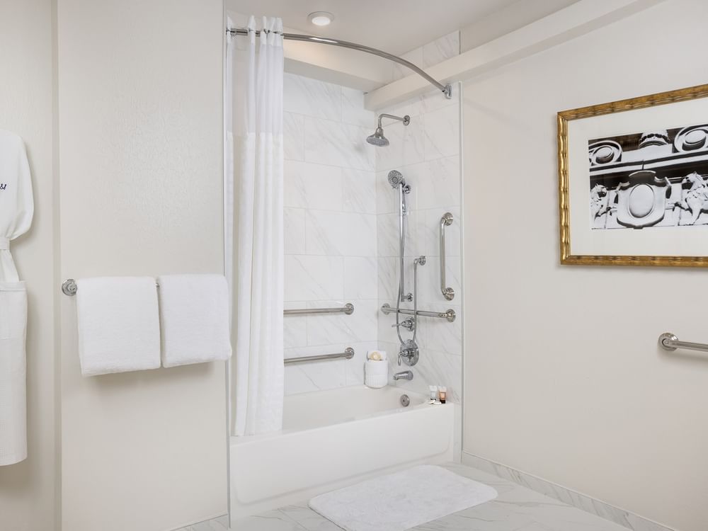Bathtub with grab bars by a white curtain under a tiled wall in Classic Double Accessible at Warwick Melrose Dallas