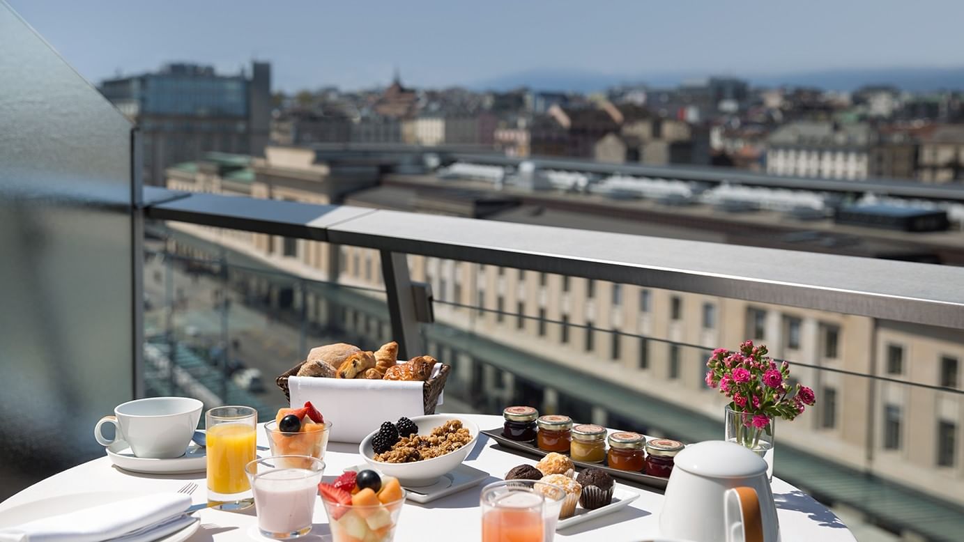 Breakfast tray with pastries and fruit by a metal railing under a clear sky at Warwick Geneva