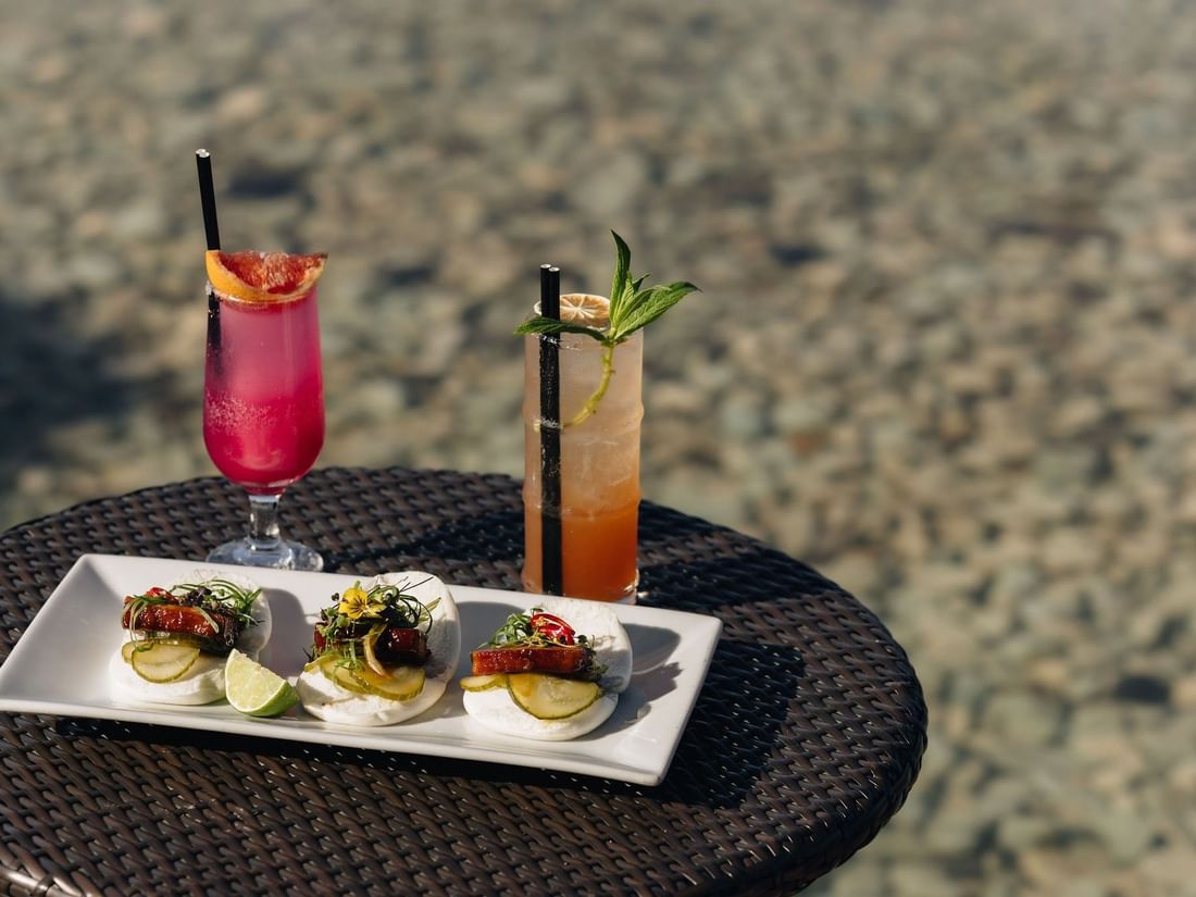 Plate of appetizers and two cocktails on a table at Pool Bar, Pullman Bunker Bay Resort