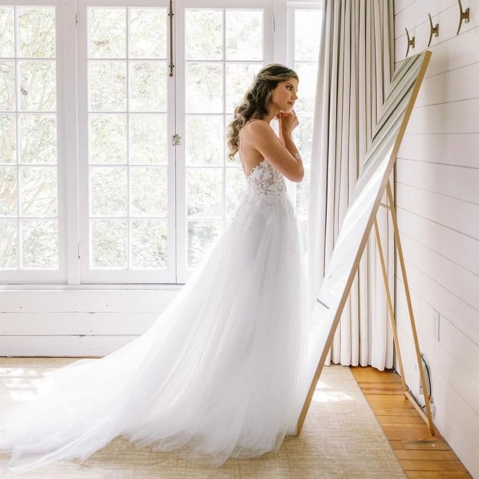 A bride stands in a white gown before a mirror, getting ready for her wedding at The Clifton Hotel in Charlottesville, VA.