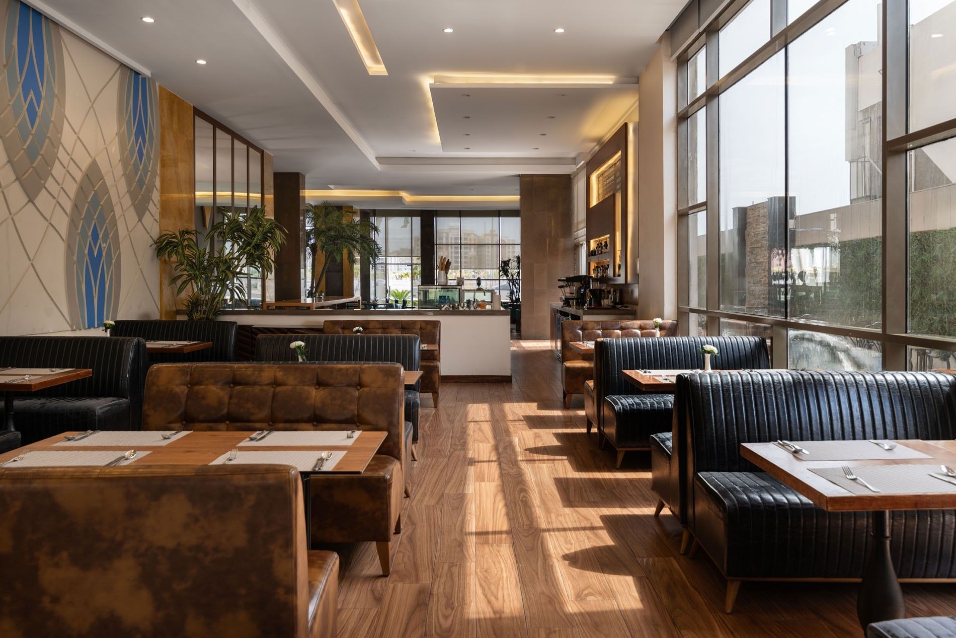 Artist Lobby Lounge with leather booths, wooden tables, and large windows letting in natural light at Warwick Hotel Jeddah
