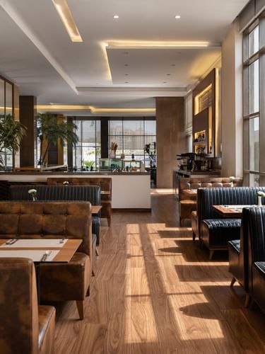 Artist Lobby Lounge with leather booths, wooden tables, and large windows letting in natural light at Warwick Hotel Jeddah
